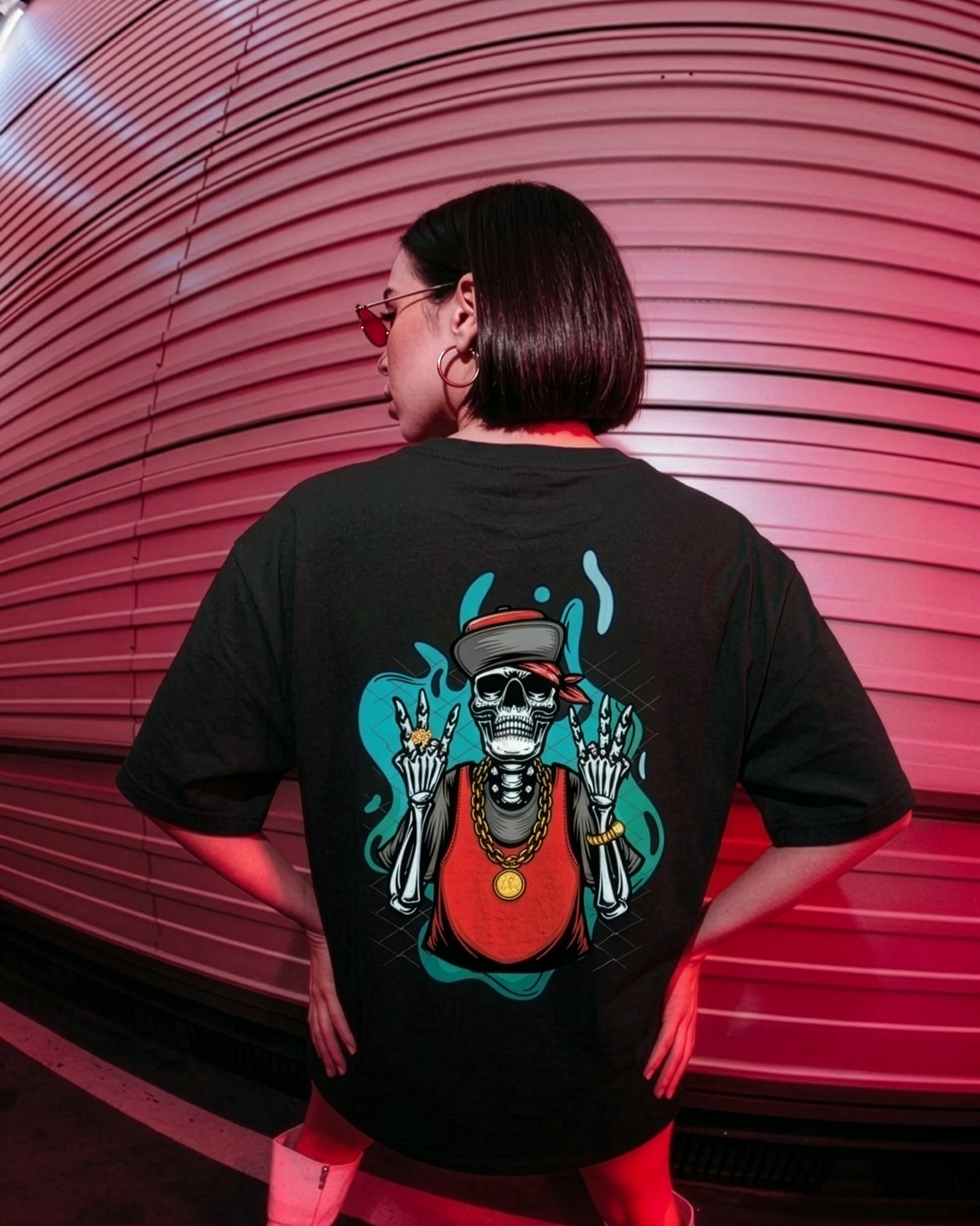 Person wearing a black t-shirt with a colorful skeleton design on the back, standing against a pink and red striped wall.