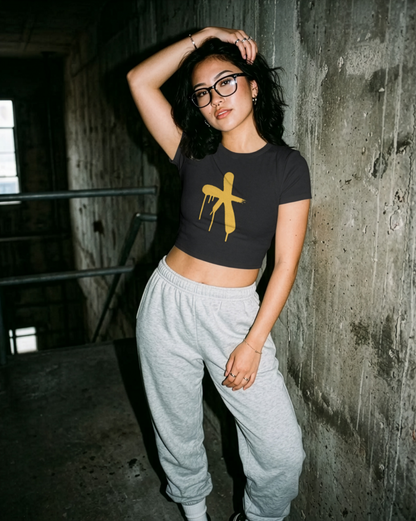 Attractive girl wearing a black crop top with a yellow graphic and grey sweatpants in an industrial rugged setting.